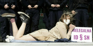 Eine junge Frau liegt ,it einem Schild auf dem Boden vor einer Reihe von Polizisten