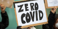 Eine Person mit einer Mund-Nasen-Maske hält ein Schild hoch, auf dem steht: "Zero Covid"