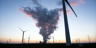 Krafwerk mit Rauchwolken umringt von Windrädern