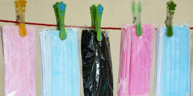 Verpackte rosa und hellblaue Medizinmasken hängen auf der Wäscheleine