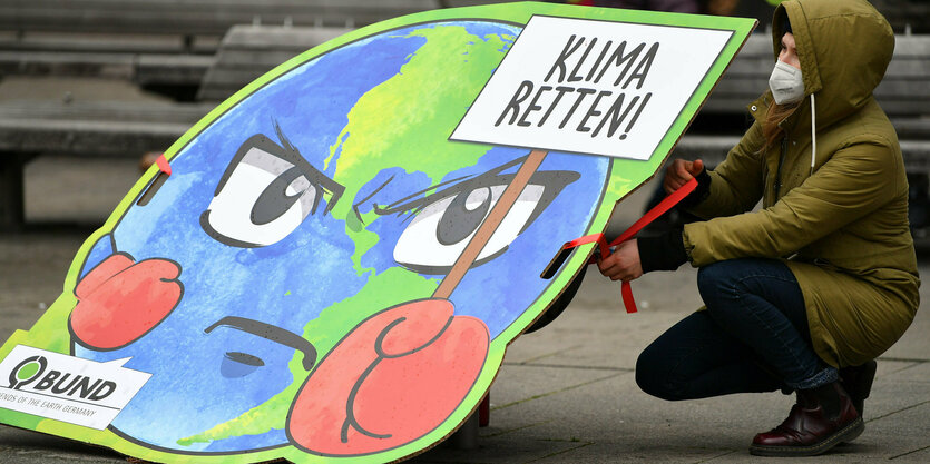 Auf dem Boden kniet eine Person mit einem Schild auf dem Klima retten steht.