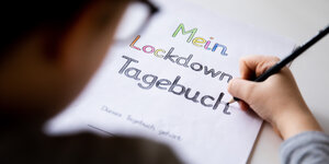 Ein Schüler malt an einem Tisch die Buchstaben eines Lockdown Tagebuchs aus