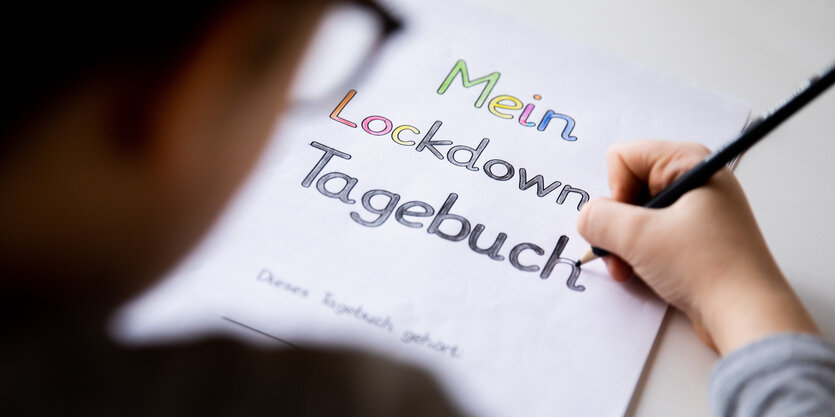 Ein Schüler malt an einem Tisch die Buchstaben eines Lockdown Tagebuchs aus