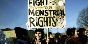 Eine Demonstrantin hält ein Schild hoch mit der Aufschrift "Fight for your menstrual rights"