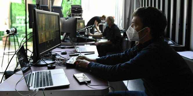 Rechner, Labtop, Festplatten stehen auf dem Tisch, davor sitzt ein junger Mann