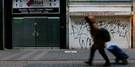 Eine Frau geht mit einem Rollkoffe eine Straße entlang. Im hintergrund sind geschlossene Geschäfte zu sehen