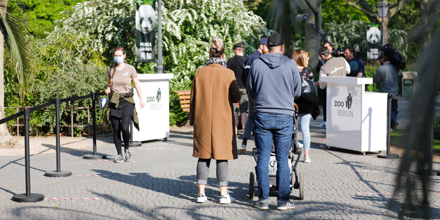 Menschen mit Masken und Kinderwagen vor einem Zoo-Eingang