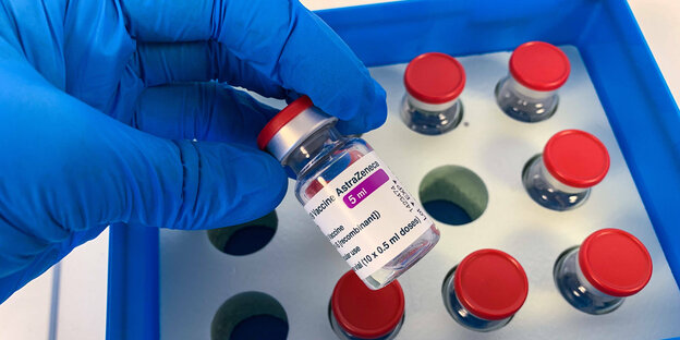 AstraZeneca Impfstoffampulle in der Hand mit medizinischen Handschuhen vor der Lieferbox