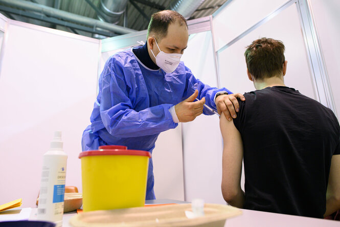 Ein Arzt impft im Impfzentrum in der Messe Dresden einen jungen Mann