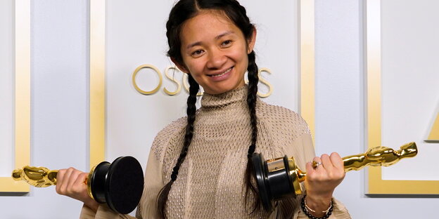 Eine Frau hält zwei Oscar- Statuen, in jeder Hand eine