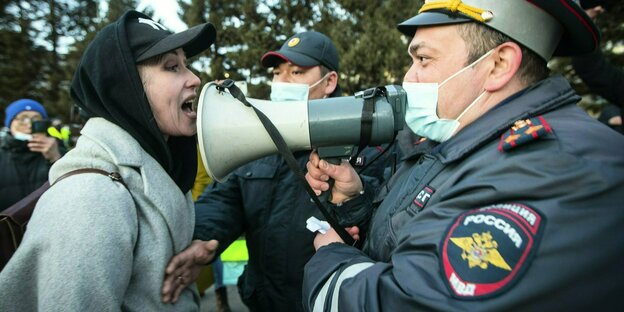 eine Demonstrantin debatiert mit einem Polizisten, der ein Megafon vor seinen Mund hält