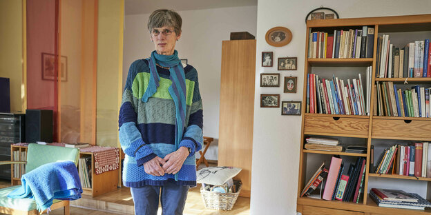 Eine Frau in blauem Pullover steht in ihrem Wohnzimmer. Die Möbel sind aus Holz
