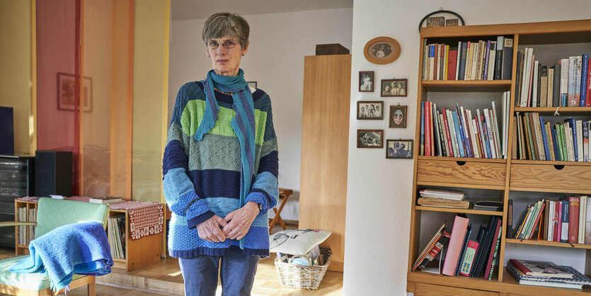 Eine Frau in blauem Pullover steht in ihrem Wohnzimmer. Die Möbel sind aus Holz