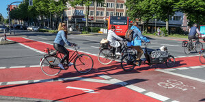 Fahrradfahrer überqueren eine Kreuzung mit breiten, rot markierten Radwegen