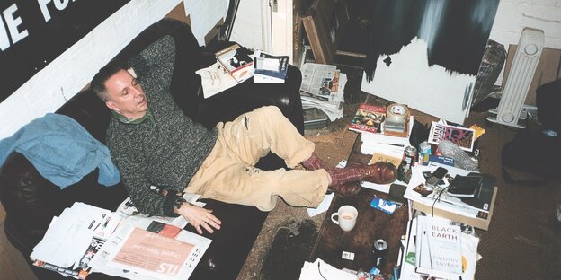 Andrew Weatherall auf einem Sofa umgeben von Büchern