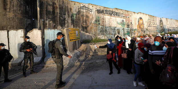 Palästinenser halten an einem Grenz-Checkpoint in Jerusalem ihre Pässe bereit - bewaffnete israelische Soldaten auf der gegenüberliegenden Seite
