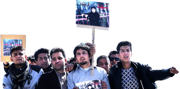 Eine Gruppe Männer hält ein Plakat der Ermordeten hoch.