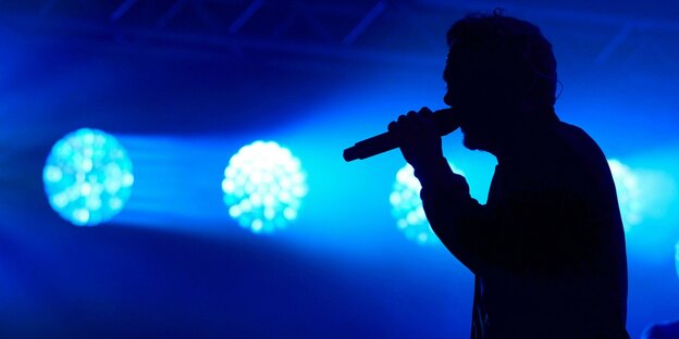 Sänger auf Bühne singt ins Mikrofon - Scheinwerfer leuchten blau