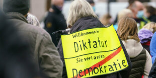 Eine Demonstrantin auf einer Querdenken-Kundgebung mit einem Schild "Willkommen in Diktatur"