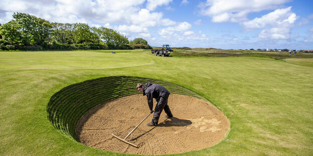 Ein Mann recht eine Sandfläche in einem Loch im Golfplatz