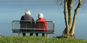 Zwei Rentnerinnen sitzen neben einem Baum auf einer Bank am Ufer