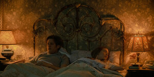 Ein Mann und eine Frau liegen im Bett. Sie schaltet gerade das Licht auf ihrer altmodischen Nachttischlampe aus.
