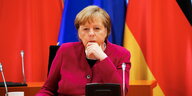 Angela Merkel sitzt vor Fahnen und schaut in einen Monitor