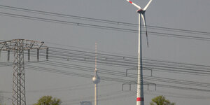 Eine Sicht auf die Stadt Berlin von Brandenburg aus, man sieht den Fernsehturm in weiter Ferne, Stromleitungen und eine Windernergieanlage