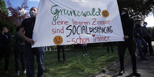 1. Mai 2020: Demonstranten der MyGruni-Kundgebung halten ein Plakat mit der Aufschrift «Grunewald, deine leeren Zimmer sind social distancing - schon immer» im Grunewald hoch