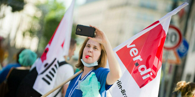Eine Pflegekraft fotografiert sich auf einer Demonstration mit ihrem Smartphone