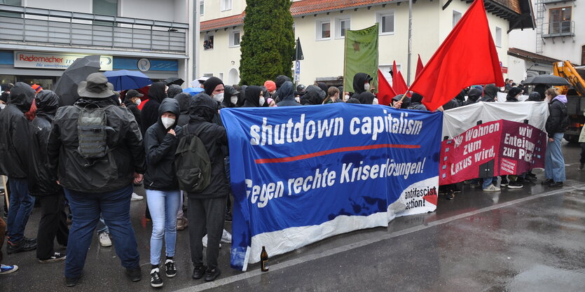 Eine größere Gruppe von Angehörigen der autonomen Szene mit großem Transpi und roten Fahnen stehen auf dem Marktplatz von Grünwald