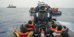 Zwei Boote treiben voller Menschen mit Rettungswesten auf dem Meer