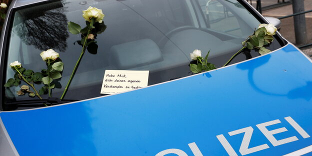 Blumen und eine Karte klemmen auf der Windschutzscheibe einer Polizeiautos. Auf der Karte steht: "Habe Mut, dich deines eigenen Verstandes zu bedienen"