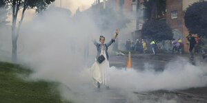 Eine Frau steht mit erhobenen Händen in einer Wolke aus Tränengas auf einer Straße
