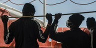 Zwei Migranten an Bord der „Ocean Viking“ mit Mund-Nasenschutz halten sich an einer Stange fest