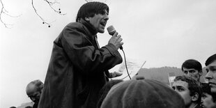 Rudi Dutschke spricht in ein Mikrofon unter freiem Himmel