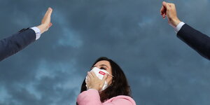 Isabel Diaz Ayuso bei einer Wahlkampfveranstaltung mit weißem Mundschutz - neben hier zwei in den Himmel gestreckte Männerarme