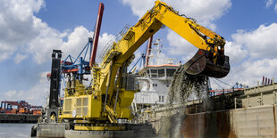 Ein Bagger auf einem Ponton hebt mit seiner Schaufel Schlick aus dem Wasser auf ein Schiff