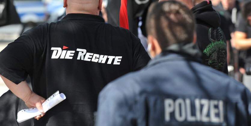 Ein Neonazi mit dem Schriftzug "Die Rechte" auf seinem Pullover steht vor einem Polizisten.