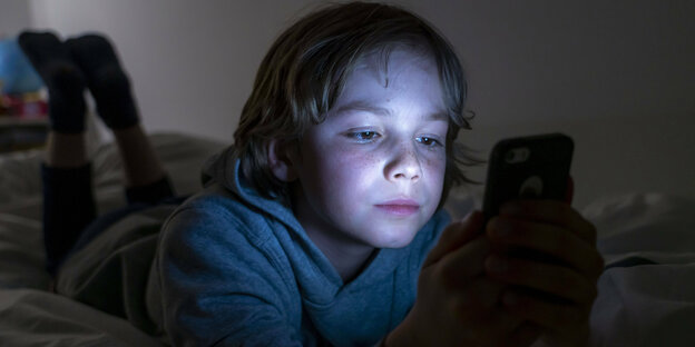 Ein Kind liegt im Bett und starrt auf ein Smartphone