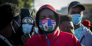 Ein Migrant aus Haiti mit einer Maske in den Farben der mexikanischen und der US-Flagge zeigt