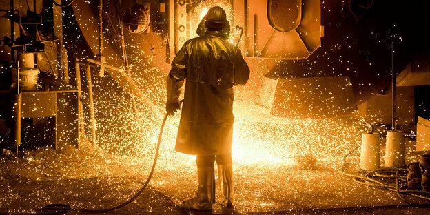 Ein Stahlarbeiter steht in Schutzkleidung an einer Stahlpfanne