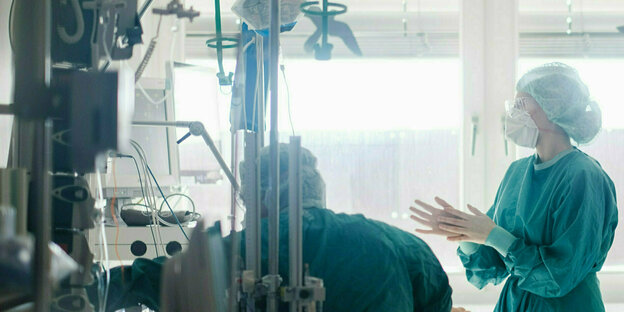 Eine Frau in Schutzkleidung steht an einem krankenhausbett, auf dem ein Patient liegt