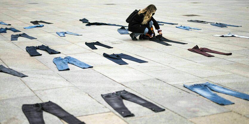 Jeans liegen auf dem Fußboden aus. Eine Frau legt eine Jeans dazu