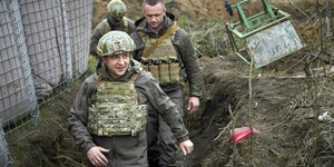 Drei Männer in Militärkluft gehen durch einen Schützengraben