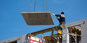 Ein Arbeiter steht auf einem Gerüst und dirigiert eine am Kran hängende Deckenplatte