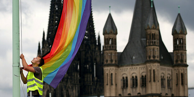 Ein Mann hisst eine Regenbogenfahne vor einer Kirche