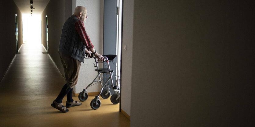 Mann mit Rollator in einem dunklen Flur.