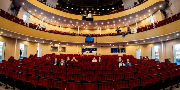 Vereinzelt sitzen Menschen mit Masken in roten Stuhlreihend des Parketts des Kieler Opernhauses