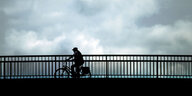 Ein Fahrradfahrer fährt vor dunklem Wolkenhimmel über eine Brücke